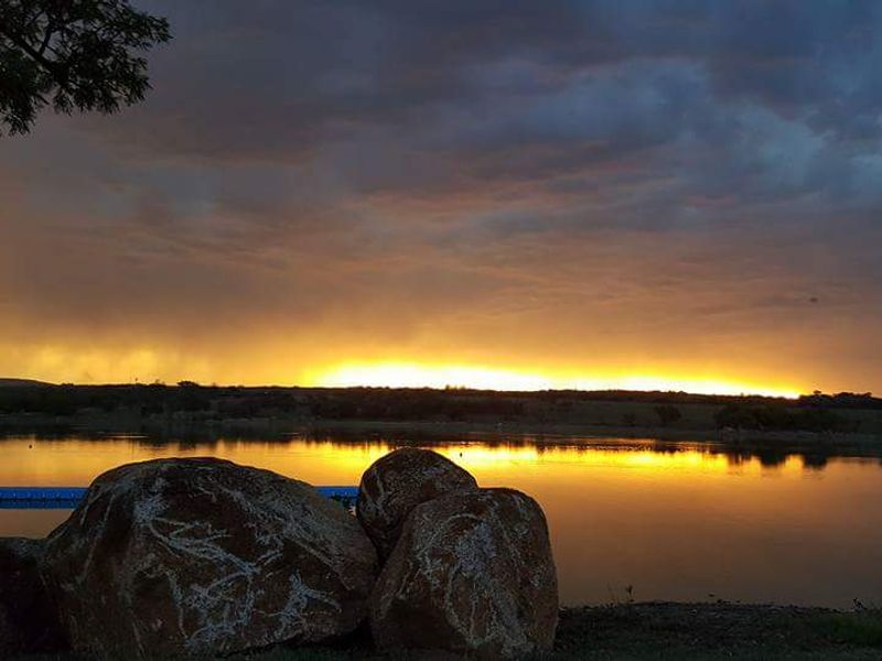 A scenic view of a tranquil lake at sunset, featuring a floating dock and natural rock formations along the shoreline.