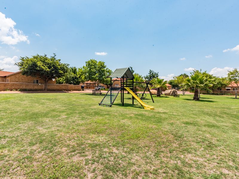 A well-maintained communal garden area featuring a large lawn and fixed playground equipment within a secure residential complex.