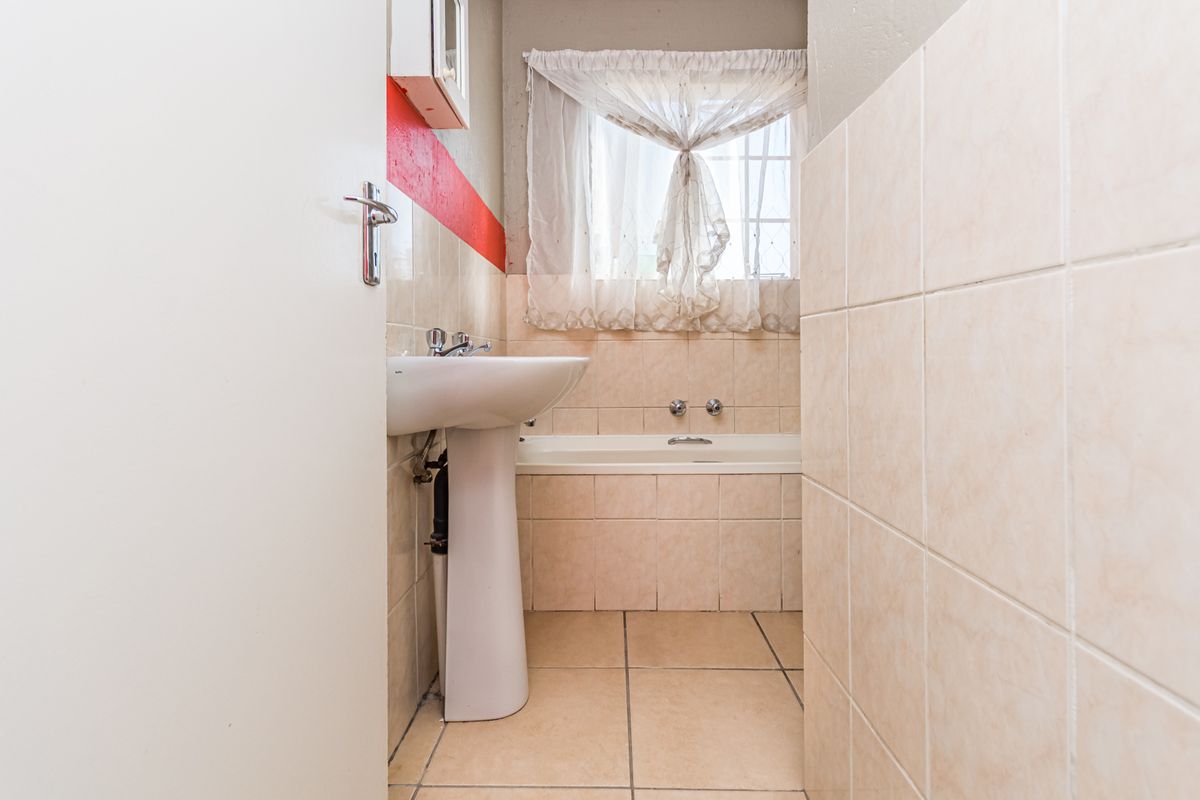 A functional bathroom featuring a pedestal basin and a built-in bathtub with neutral ceramic tiling throughout.
