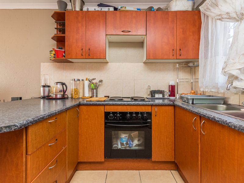 A functional kitchen featuring wooden cabinetry, laminate countertops, a built-in oven with electric hob, and a tiled backsplash.