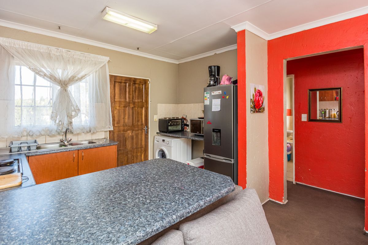 A functional kitchen featuring laminate countertops, built-in cabinetry, and a stainless steel sink, with direct access to an adjacent room.