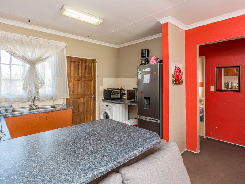 A functional kitchen featuring laminate countertops, built-in cabinetry, and a stainless steel sink, with direct access to an adjacent room.