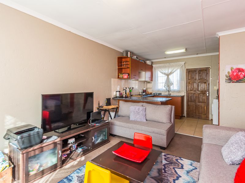 Open-plan living area featuring a compact kitchen with built-in cabinetry and tiled flooring, leading to a timber entrance door.