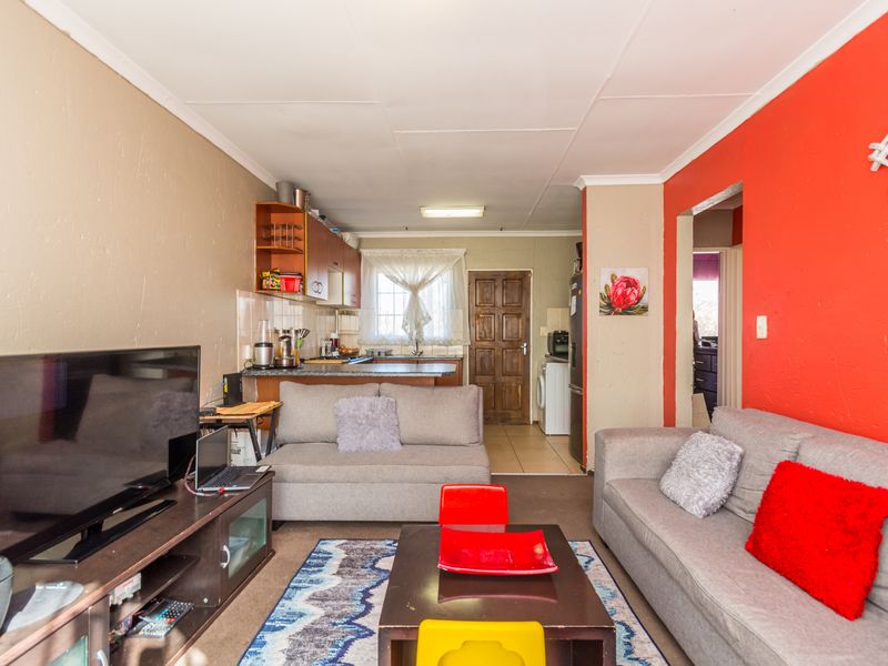 Open plan living area featuring a compact kitchen with cabinetry and tiled flooring, leading to a comfortable lounge space.