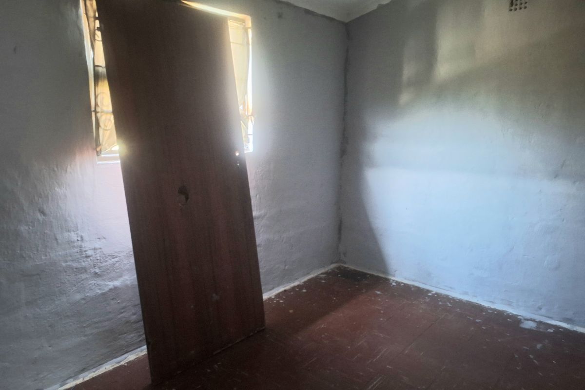 An empty bedroom featuring basic finishes, a window with security bars, and a ventilation brick. The room requires cosmetic updates and repairs.