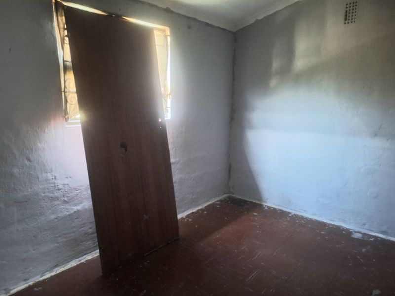 An empty bedroom featuring basic finishes, a window with security bars, and a ventilation brick. The room requires cosmetic updates and repairs.