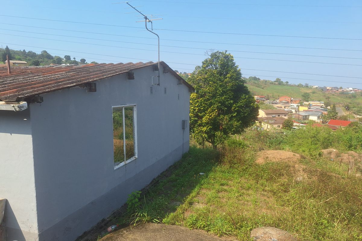 Rear view of the property showing the exterior wall, corrugated roof, and surrounding garden area with a view of the neighborhood.
