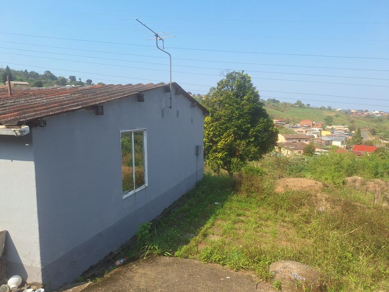 Rear view of the property showing the exterior wall, corrugated roof, and surrounding garden area with a view of the neighborhood.
