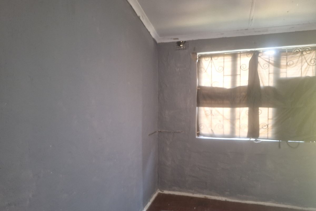 An empty bedroom featuring security burglar bars on the window and visible wall surface imperfections requiring cosmetic attention.