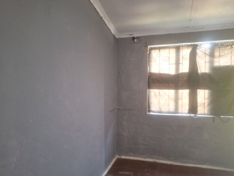 An empty bedroom featuring security burglar bars on the window and visible wall surface imperfections requiring cosmetic attention.