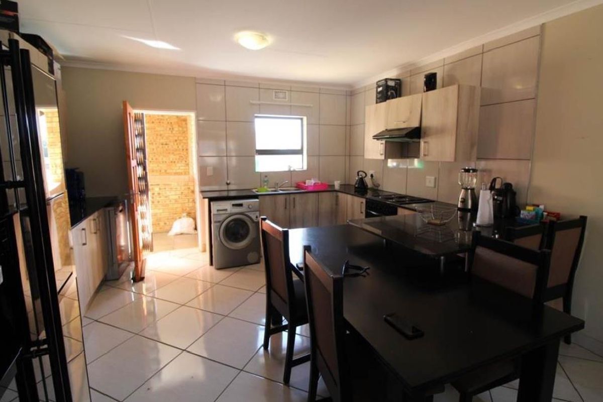 A functional kitchen featuring tiled flooring, built-in cabinetry, a tiled backsplash, and integrated appliance connections, with an adjacent doorway leading to an exterior area.