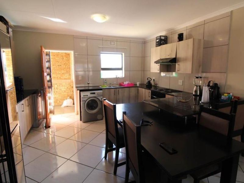 A functional kitchen featuring tiled flooring, built-in cabinetry, a tiled backsplash, and integrated appliance connections, with an adjacent doorway leading to an exterior area.