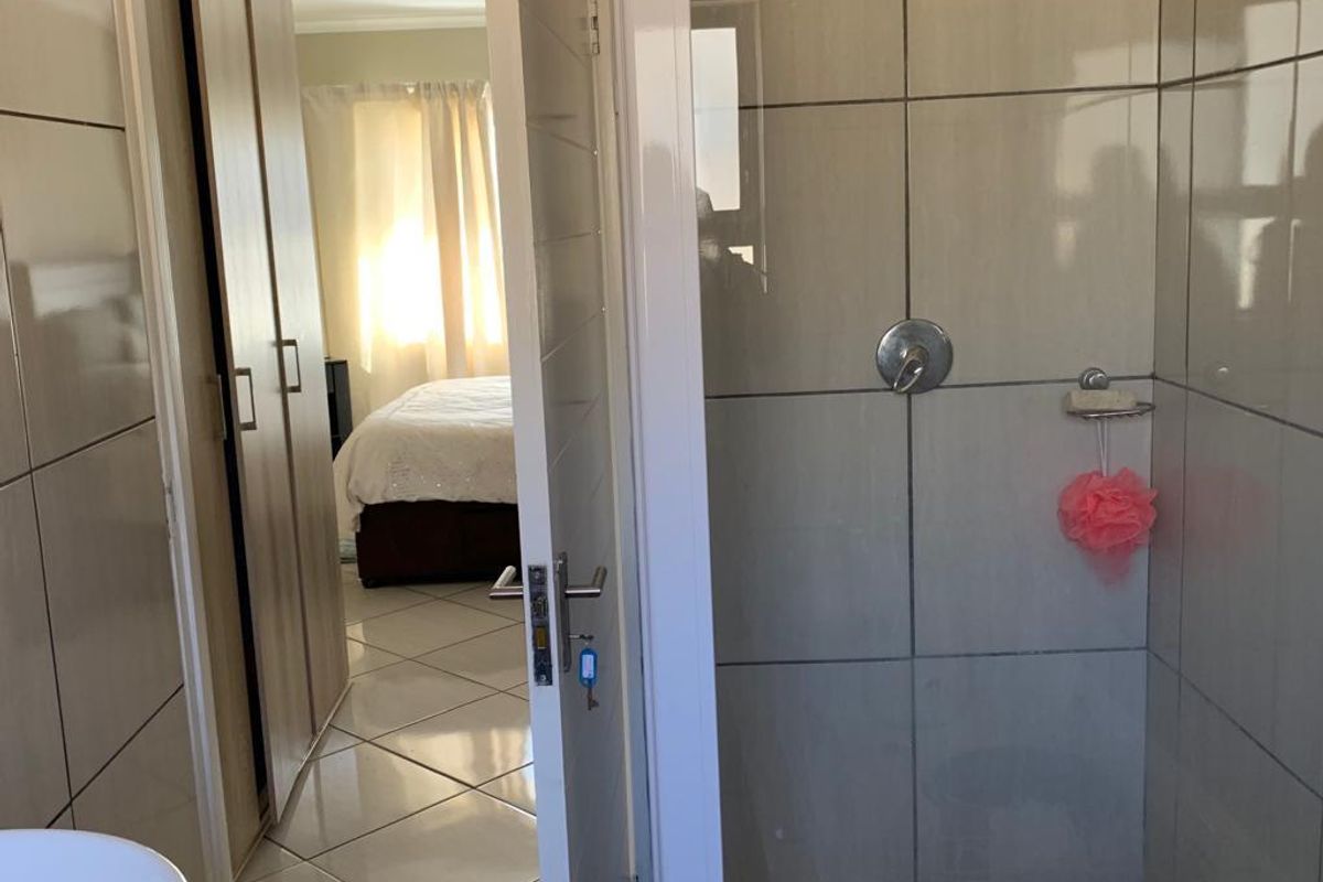 A modern bathroom featuring a glass-enclosed shower with tiled walls, a vessel sink on a granite vanity, and tiled flooring.