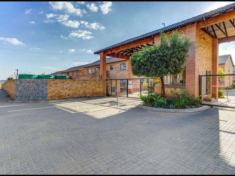 The entrance to Brentwood Manor featuring a secure gated access point, brick facade architecture, and a paved driveway.