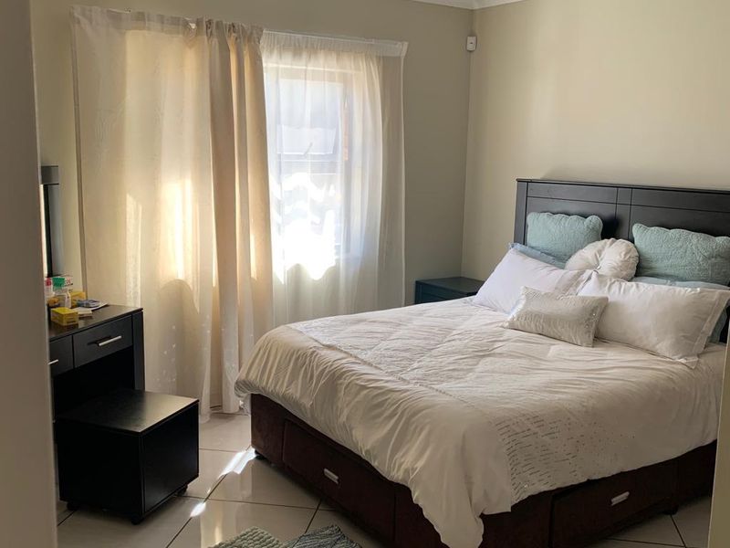 A well-lit bedroom featuring neutral wall tones, tiled flooring, and large windows with curtain treatments, providing a comfortable and functional living space.