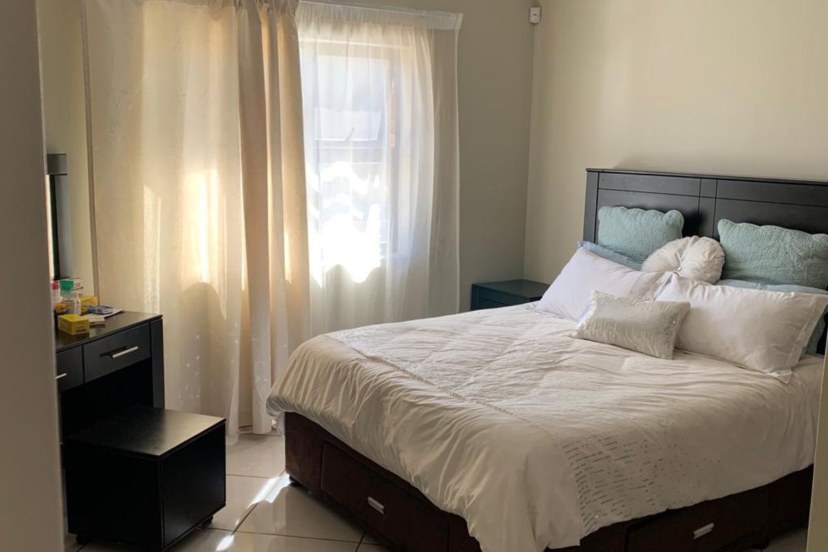 A well-lit bedroom featuring neutral wall tones, tiled flooring, and large windows with curtain treatments, providing a comfortable and functional living space.