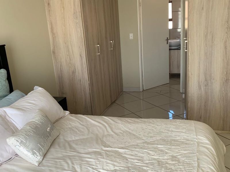 A bedroom featuring light wood-finish built-in cupboards and tiled flooring, with a view through to an adjoining bathroom.