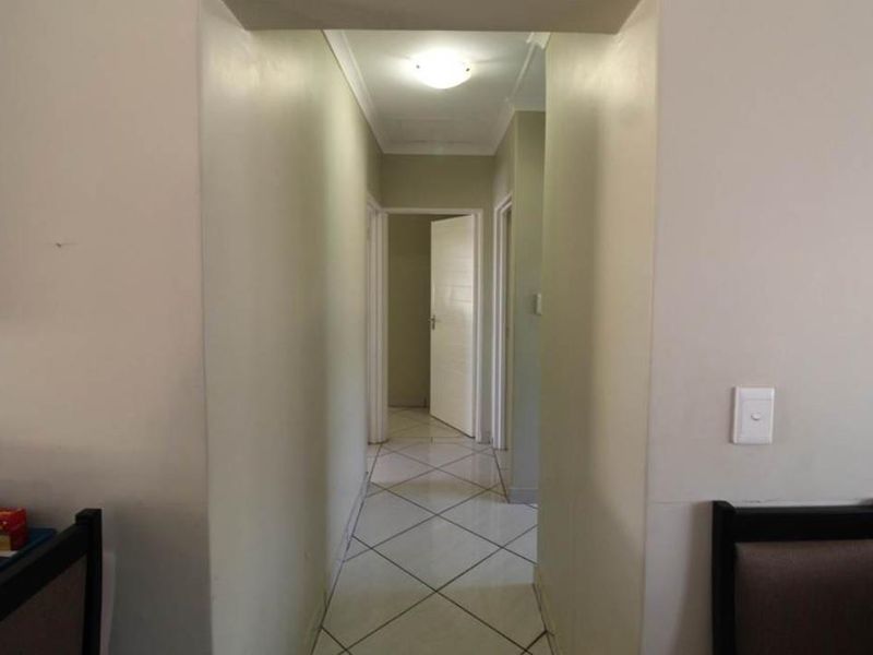 A clean, neutral-toned hallway featuring tiled flooring and access to multiple rooms through internal doors.