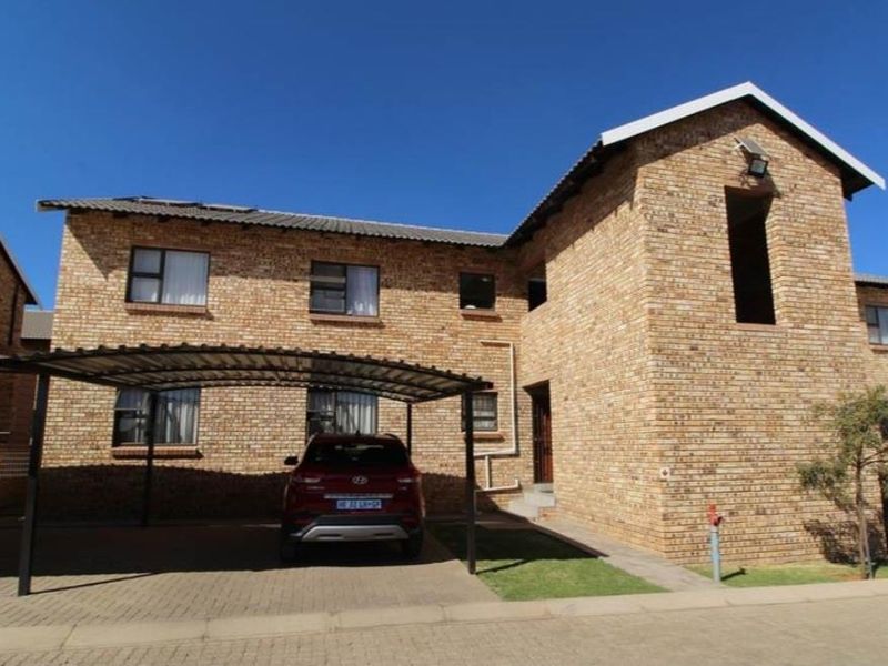 Front exterior view of a face brick apartment building featuring a covered carport and paved driveway area.
