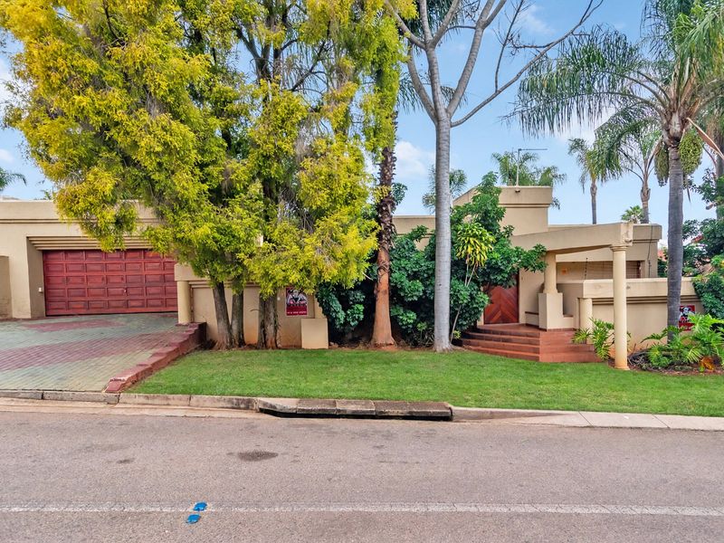 Front elevation of a duet property featuring a paved driveway, double wooden garage door, and a covered entrance with landscaped garden.