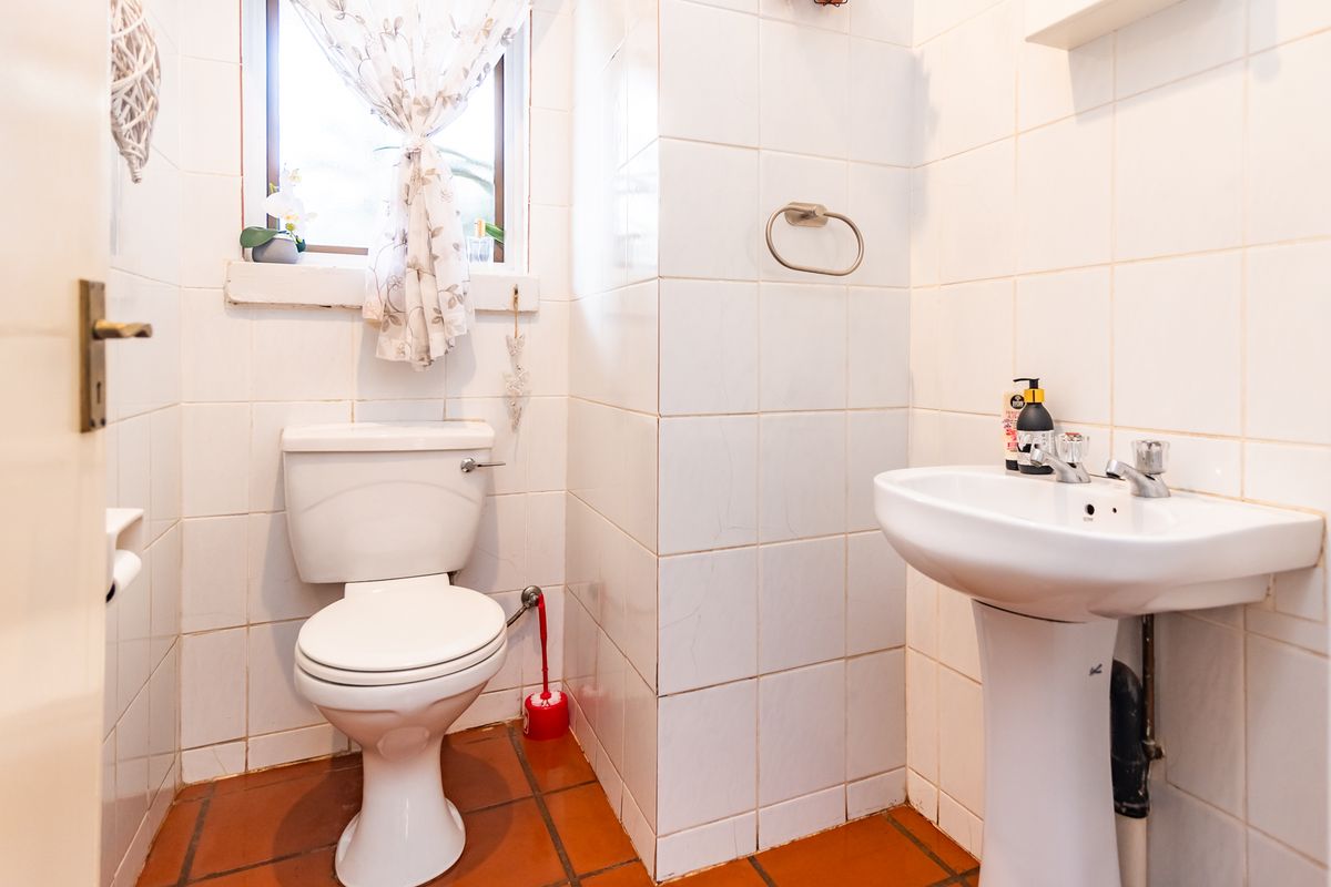 A compact bathroom featuring a pedestal basin, toilet, and tiled finishes. The space would benefit from modern updates to the tiling and fixtures.