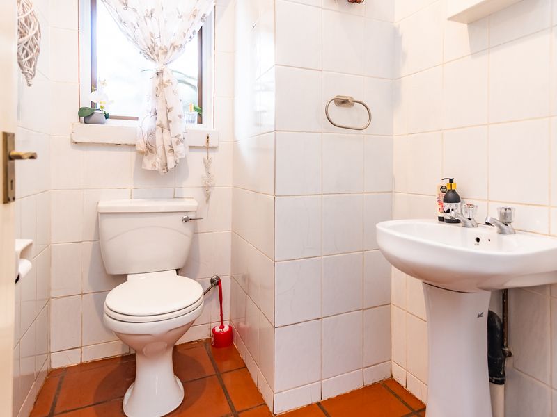 A compact bathroom featuring a pedestal basin, toilet, and tiled finishes. The space would benefit from modern updates to the tiling and fixtures.