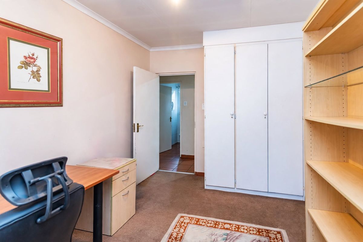 A functional bedroom featuring built-in cupboards, carpeted flooring, and direct access to an adjoining room.