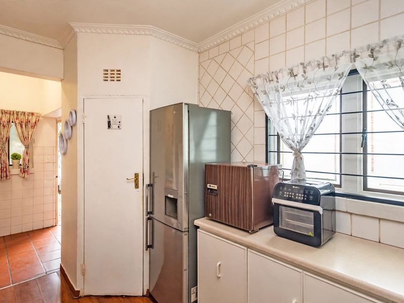 A functional kitchen area featuring tiled splashbacks, built-in cabinetry, and a window with security bars, offering a practical layout for daily use.