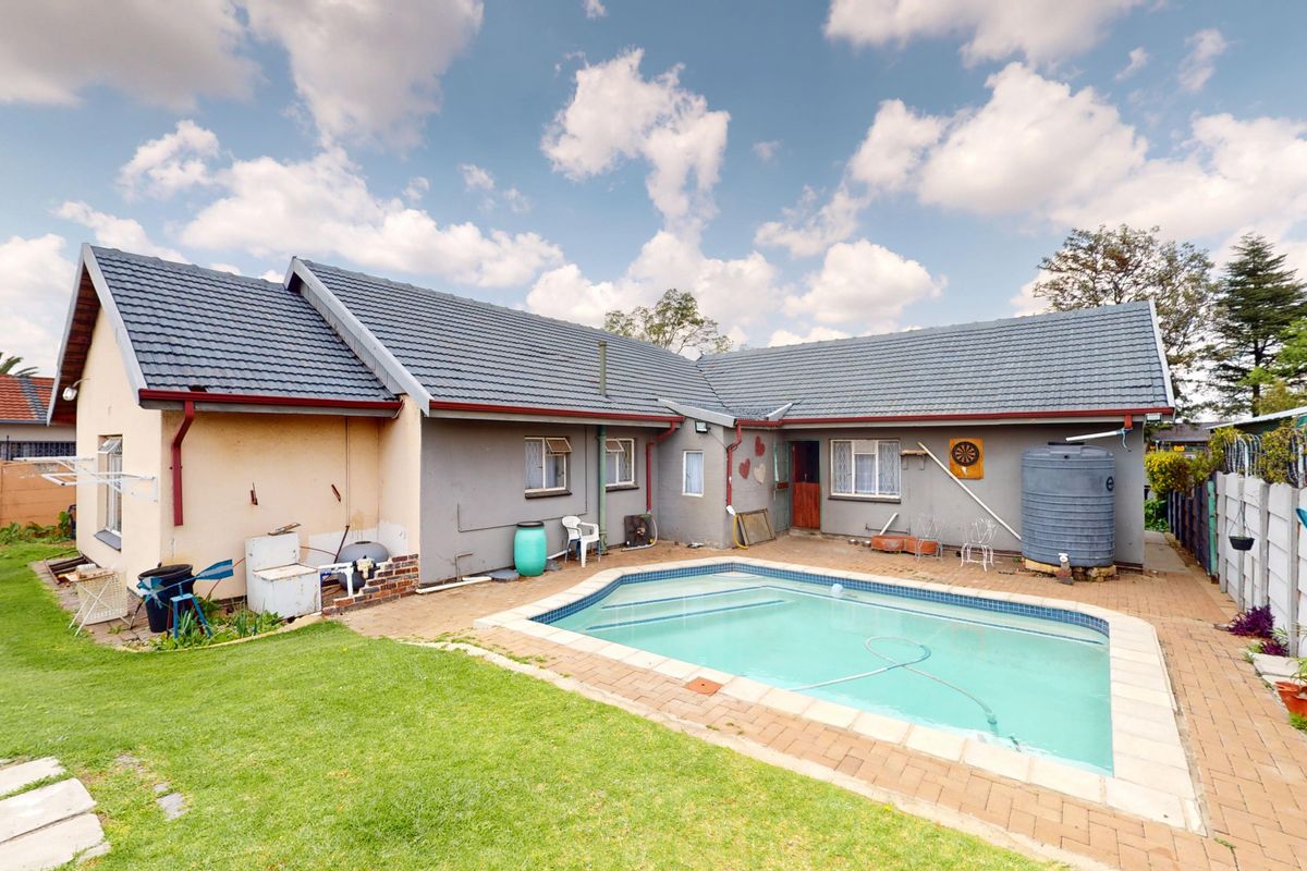 Rear exterior view of the house featuring a swimming pool, paved patio area, and a water tank set against a grassed garden.