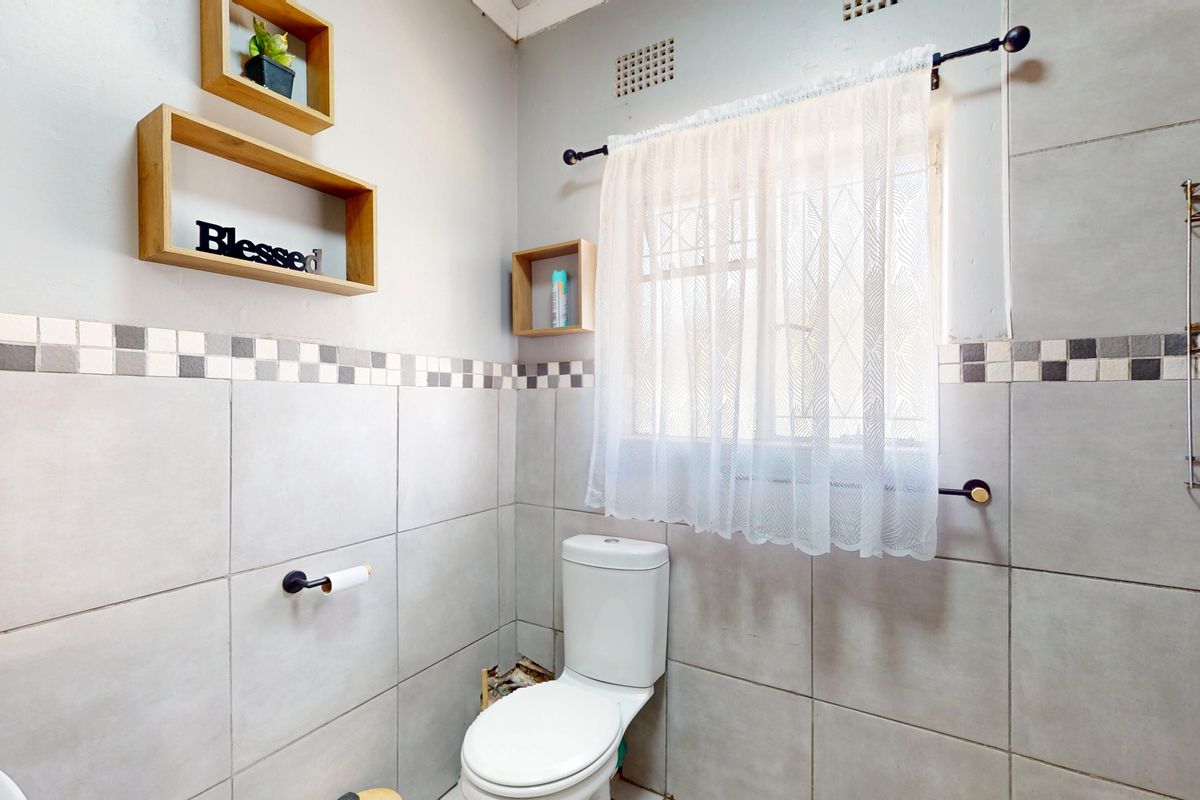 A functional bathroom featuring neutral ceramic wall tiles, a standard toilet, and a window with security bars.