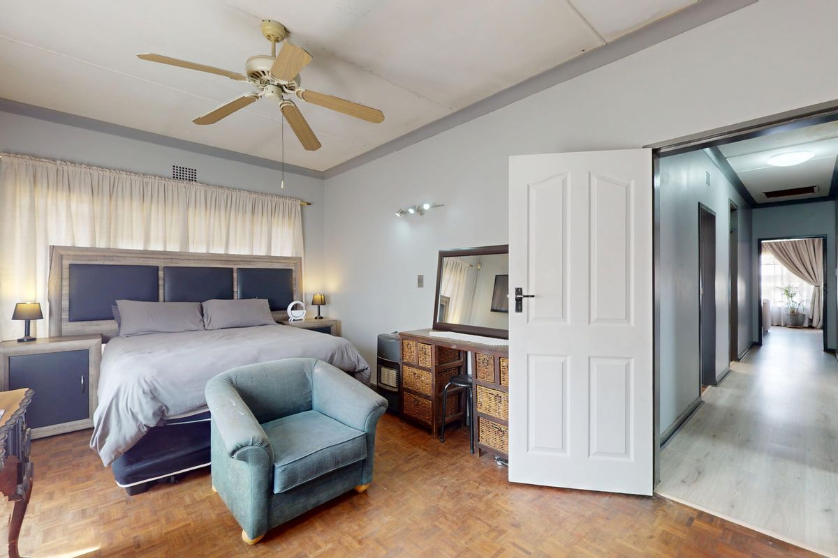 Spacious bedroom featuring classic parquet flooring, a ceiling fan, and a built-in headboard, offering a functional layout with direct access to the hallway.