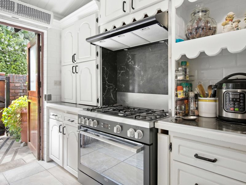 A functional kitchen featuring white cabinetry, a gas stove with extractor fan, marble-look splashback, and direct access to an outdoor patio area.