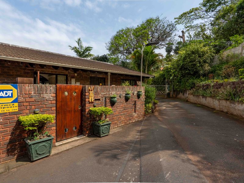 Front exterior view of the townhouse featuring a brick boundary wall, wooden pedestrian gate, and paved driveway access.