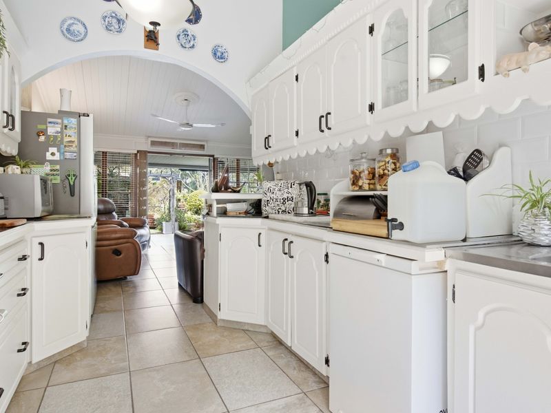 Open-plan kitchen featuring white cabinetry, subway tile backsplash, and ceramic flooring, flowing seamlessly into the adjacent living area through a classic arched opening.