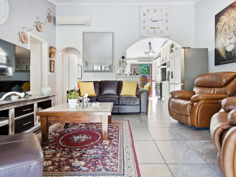 Open-plan living area featuring tiled flooring, a split-system air conditioner, and an arched transition leading into the kitchen space.