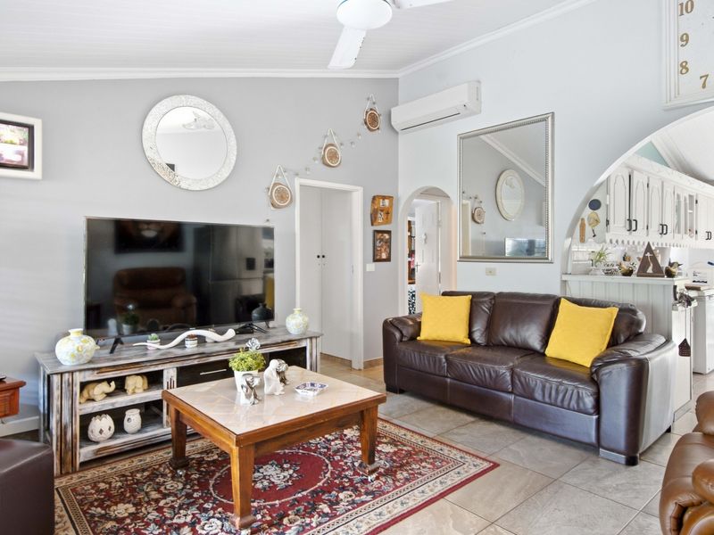 Open-plan living area featuring tiled flooring, a ceiling fan, and a split-system air conditioner, with an arched transition to the kitchen space.