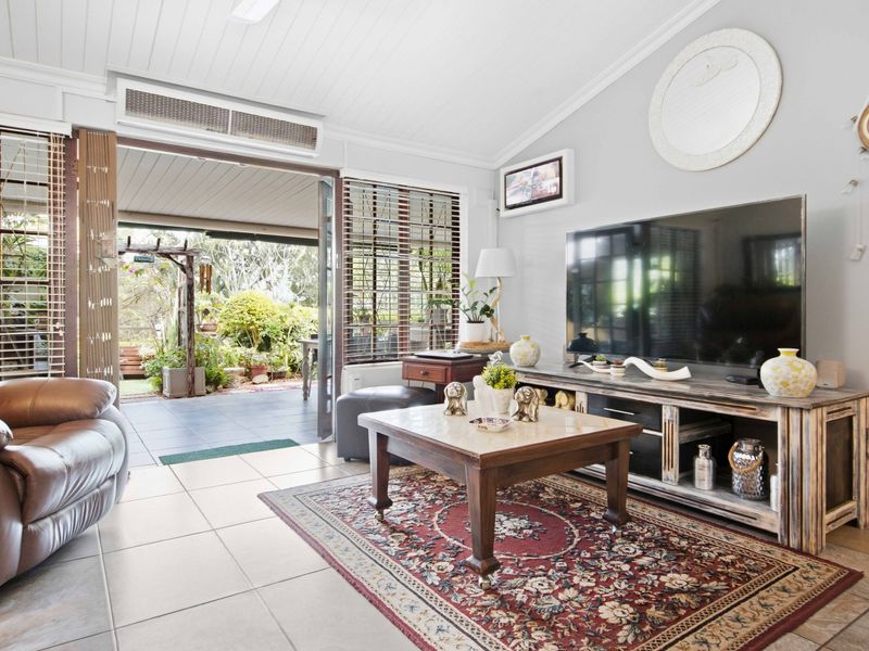 A bright living room featuring tiled floors, ducted air conditioning, and large sliding doors that open onto a covered outdoor patio area.
