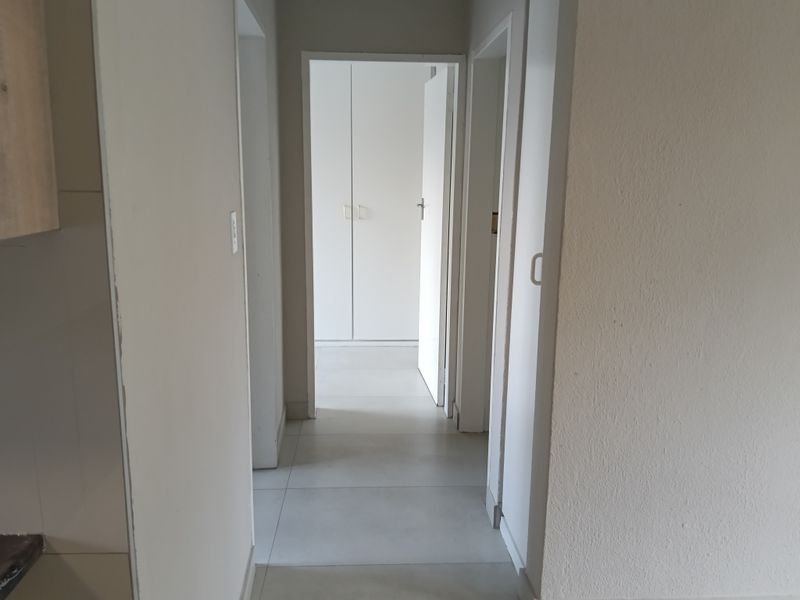 A clean, neutral hallway featuring tiled flooring and built-in storage cupboards, providing access to adjacent rooms within the apartment.