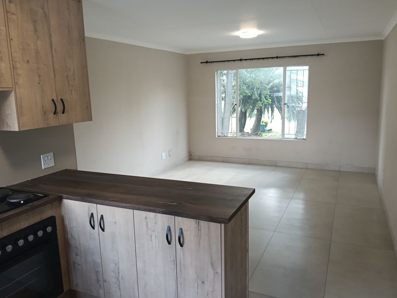 An open-plan living and kitchen area featuring modern wood-look cabinetry, built-in oven, tiled flooring, and large windows with security bars.