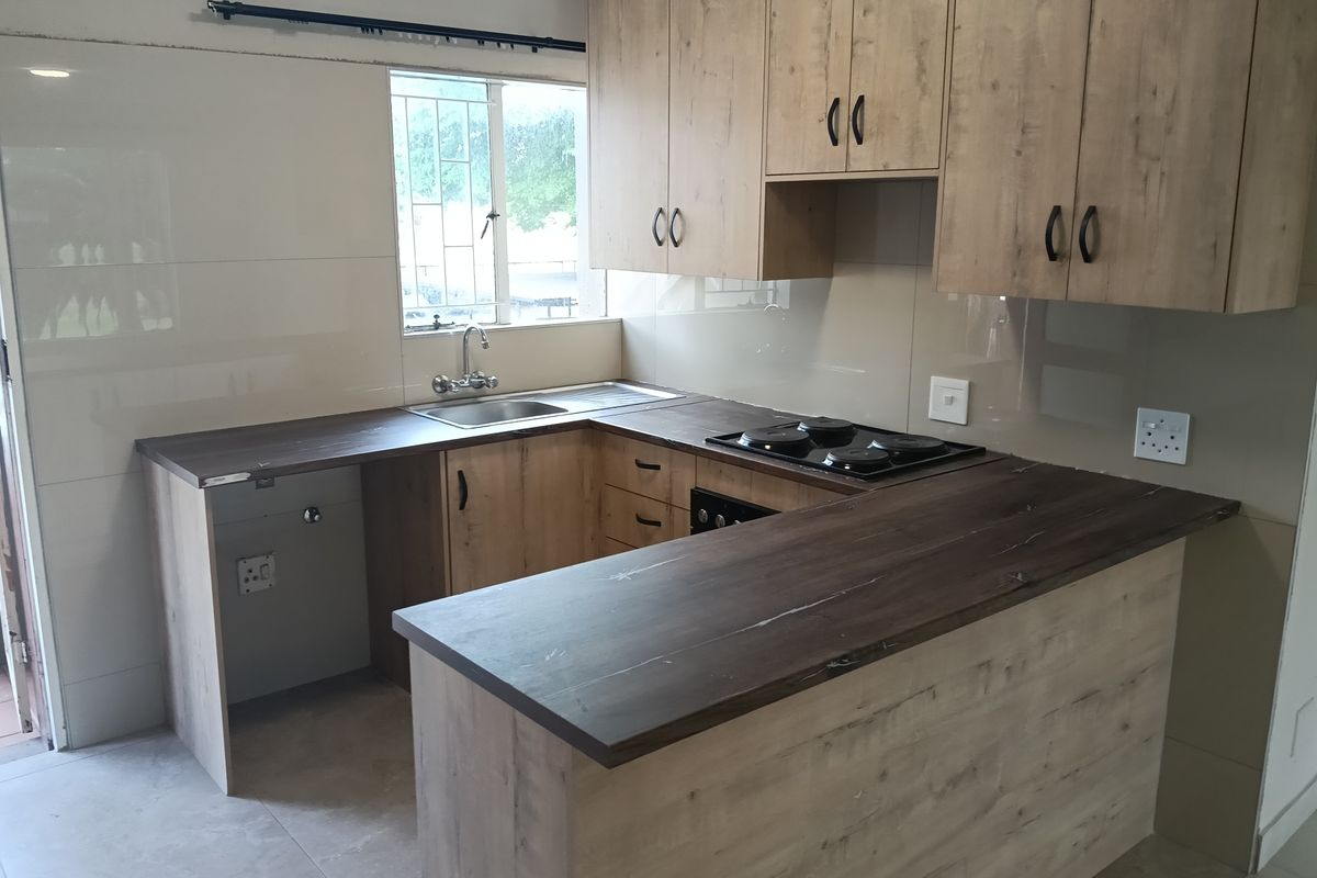 Modern kitchen featuring wood-look cabinetry, dark laminate countertops, integrated electric hob and oven, and tiled splashbacks in a clean, functional layout.