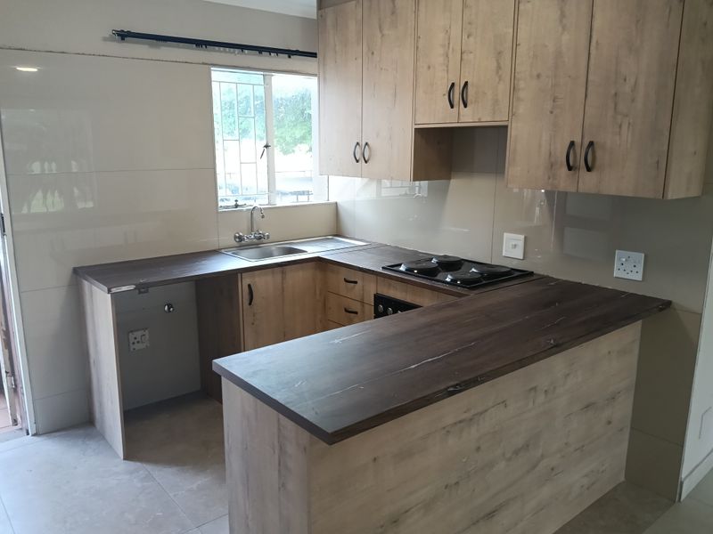 Modern kitchen featuring wood-look cabinetry, dark laminate countertops, integrated electric hob and oven, and tiled splashbacks in a clean, functional layout.