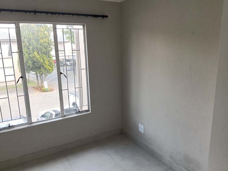 An empty bedroom featuring tiled flooring, security bars on the window, and neutral wall finishes, ready for personalization.