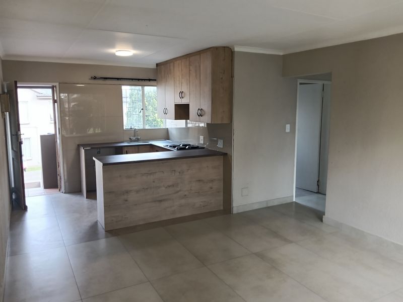 Open-plan kitchen and living area featuring modern wood-look cabinetry, tiled flooring, and a functional breakfast bar layout.