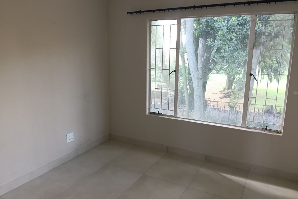 An empty bedroom featuring neutral tiled flooring, a large window with security bars, and a curtain rail, offering a blank canvas for personalization.