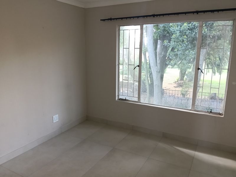 An empty bedroom featuring neutral tiled flooring, a large window with security bars, and a curtain rail, offering a blank canvas for personalization.