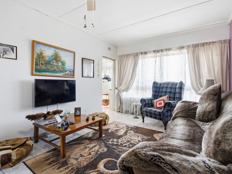 A living room featuring tiled flooring and a ceiling fan, with large windows providing natural light through existing curtain fixtures.