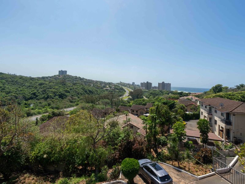 Elevated panoramic view overlooking the surrounding residential neighborhood, lush greenery, and distant coastline.