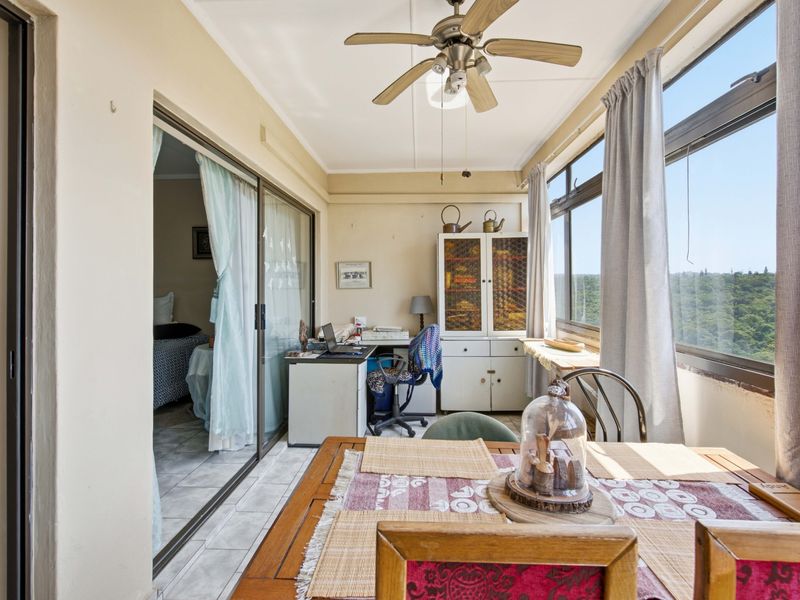 Enclosed balcony or sunroom featuring tiled flooring, a ceiling fan, and large windows offering natural light and exterior views.