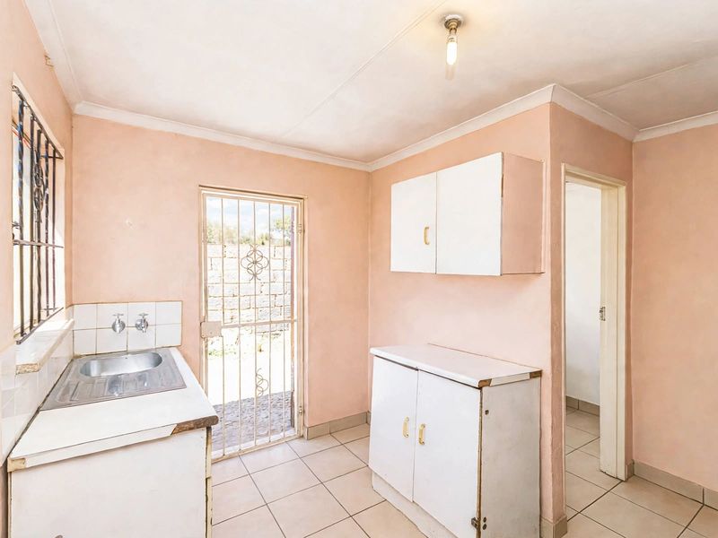 A functional scullery area featuring built-in cabinetry, a stainless steel sink, tiled flooring, and direct access to the exterior via a security gate.