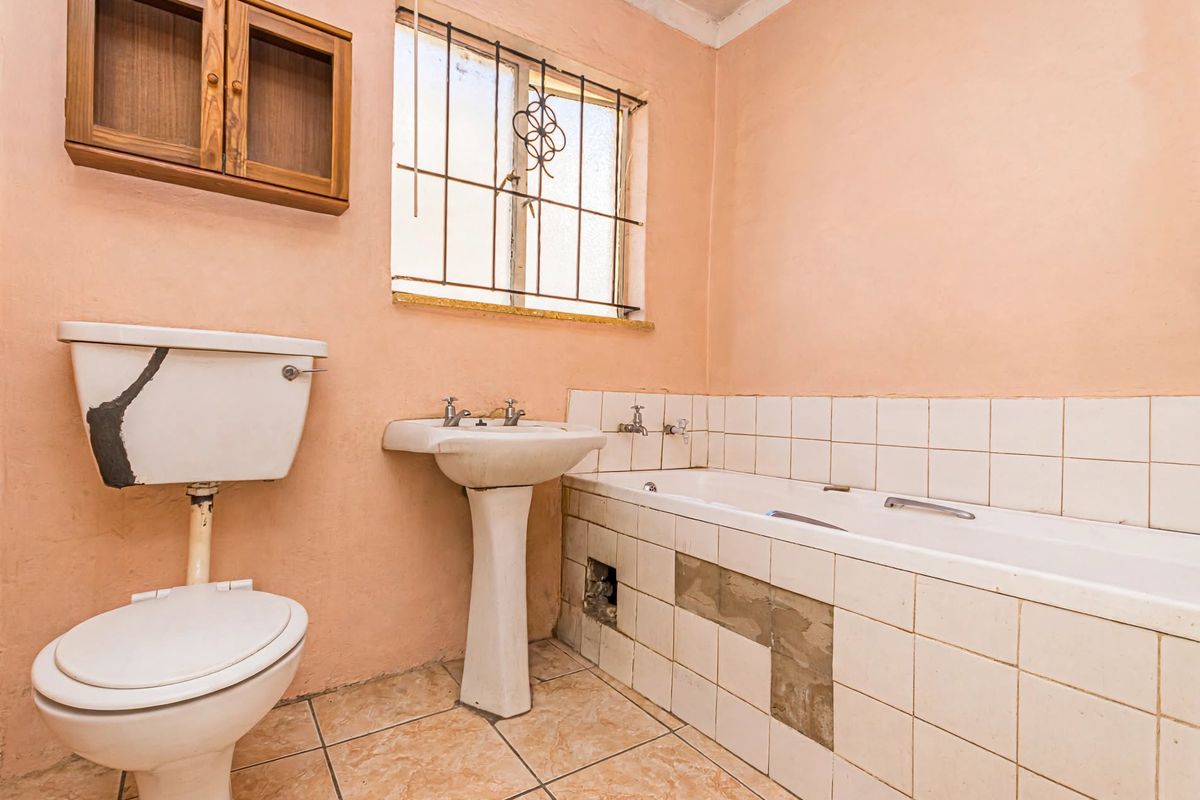 A dated bathroom featuring a pedestal basin, built-in bathtub, and ceramic tiling, currently requiring significant maintenance and cosmetic updates to restore its functionality.